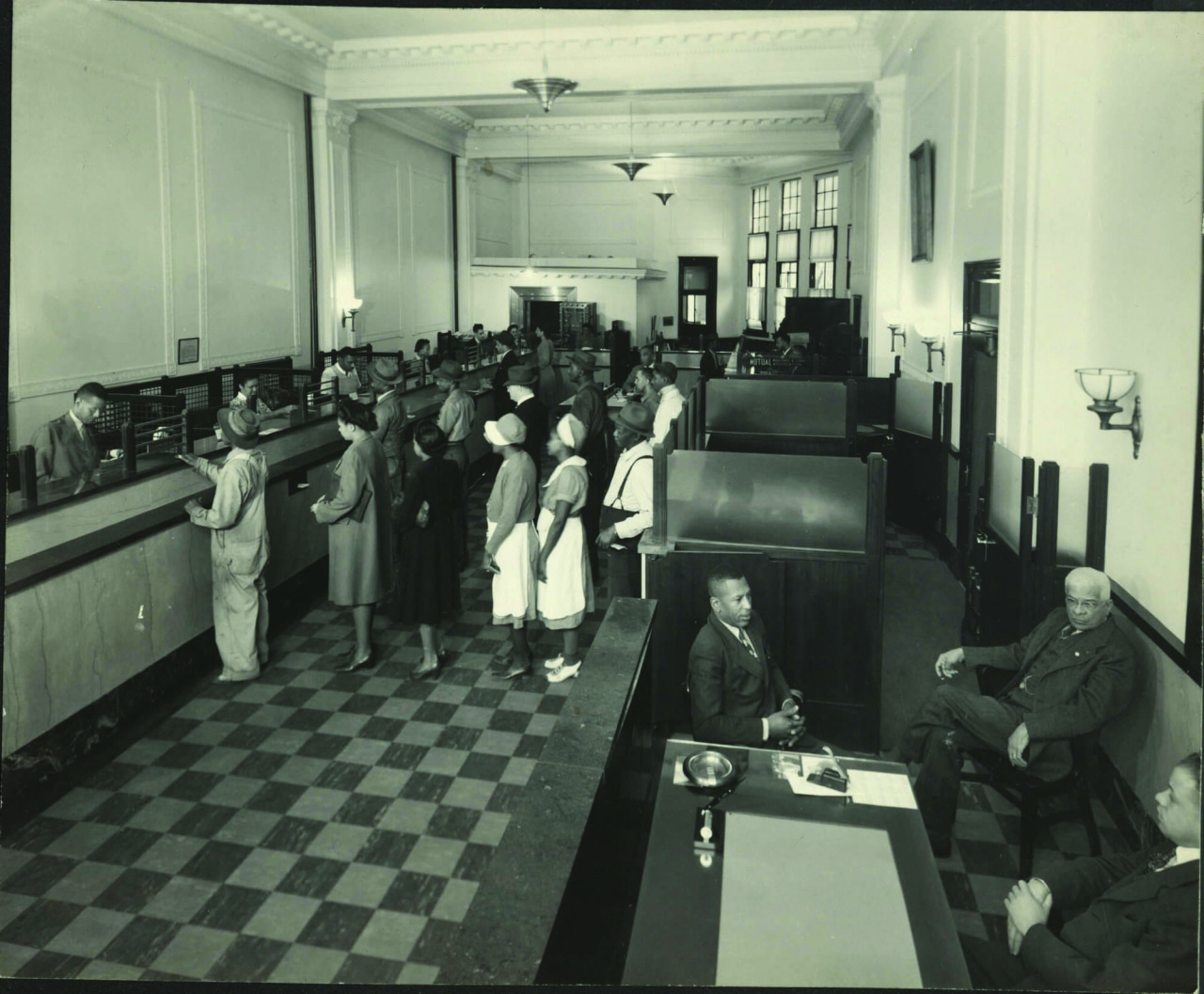 Interior of Mechanics & Farmers Bank 1930s. You can see the presence and distinctive clothing of Black farmers, laborers, domestic workers, and the middle-class professionals. Courtesy North Carolina Mutual Life Insurance Company Archives, David M. Rubenstein Rare Book & Manuscript Library, Duke University, and University Archives, Records and History Center, North Carolina Central University